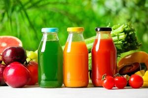 Botellas con jugos saludables, frutas y verduras en la mesa al aire libre, primer plano