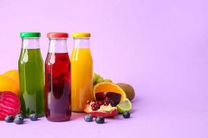 Botellas con jugos saludables, frutas y verduras sobre fondo de color foto