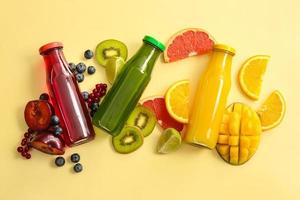 Bottles with healthy juice and fruits on color background photo