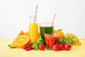 Glasses with healthy juice, fruits and vegetables on light background photo