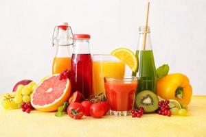 Bottles with healthy juice, fruits and vegetables on light background photo