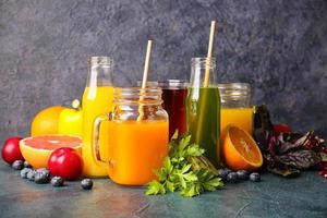 Botellas con jugos saludables, frutas y verduras sobre fondo oscuro foto