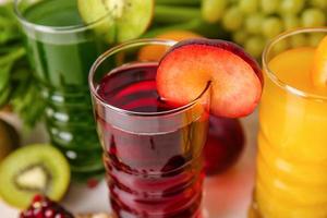 Vasos con jugos saludables, frutas y verduras sobre fondo claro