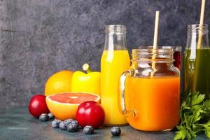 Bottles with healthy juice, fruits and vegetables on dark background photo