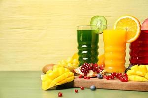 Glasses with healthy juice, fruits and vegetables on color wooden background photo