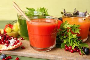 Glasses with healthy juice, fruits and vegetables on color wooden background photo