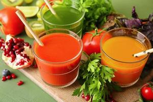Glasses with healthy juice, fruits and vegetables on color wooden background photo