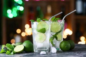 Glasses of cold mojito on table against blurred lights photo