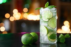 Glass of cold mojito on table against blurred lights photo