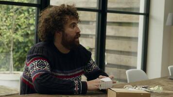 Man at table folding cardboard box whilst talking video