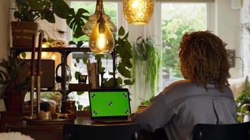 kvinna som sitter vid bordet har videosamtal med grön skärm