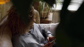 Woman sitting on sofa watching smartphone whilst pointing and talking video
