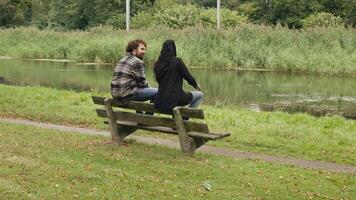 Woman and man talking whilst sitting on bench at pond video