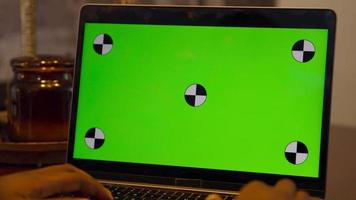 Man moving hands above keys of laptop with green screen video
