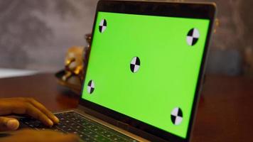 Man moving hands above keys of laptop with green screen video