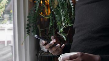 Man at window typing on smartphone and sipping drink video