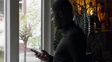 Hombre en la ventana escribiendo en el teléfono inteligente y mirando video