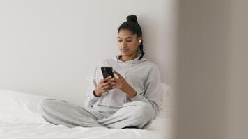 Woman sitting on bed touching screen smartphone video