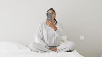 mulher sentada na cama fazendo videochamada com smartphone video
