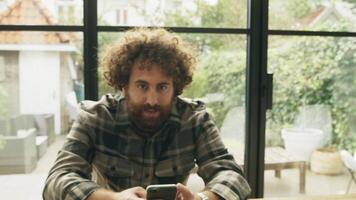 Man at table with smartphone looking up friendly into camera lens video