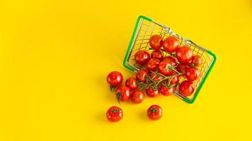 tomates cherry esparcidos en una canasta sobre un fondo amarillo brillante con un lugar vacío para una inscripción. foto