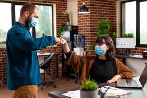 Businessman with medical face mask against covid19 greeting manager woman giving first bump photo