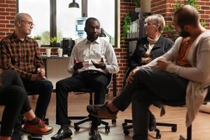 Hombre afroamericano hablando con personas y terapeuta en una reunión de grupo foto