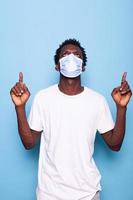 Casual man with face mask against coronavirus pointing fingers up