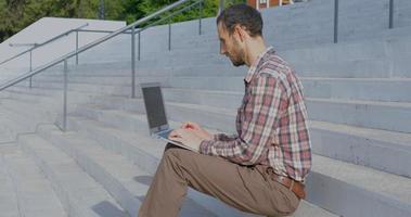 Hombre joven empresario sentado en las escaleras al aire libre trabajando con un portátil foto