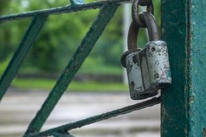 Old closed gray padlock on a green fence photo