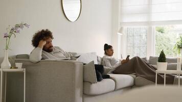 Hombre leyendo una revista y una mujer desplazándose en el teléfono inteligente ambos sentados en el sofá video