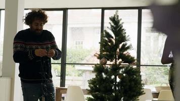 El hombre desenreda el cable y la mujer decorando el árbol de navidad con chuchería video