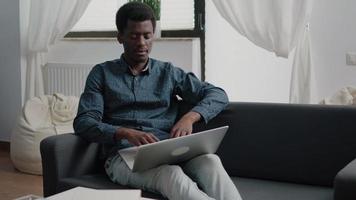 ontspannen op de bank, Afro-Amerikaanse man typen en werken met moderne laptopcomputer video