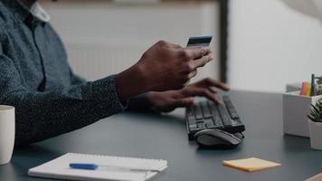 Cerca del hombre afroamericano manos escribiendo información de tarjeta de crédito en el teclado de la computadora