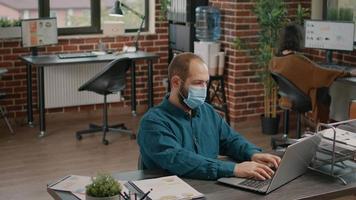 Portrait of business man with face mask working with laptop video