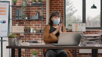 Cheerful woman with face mask reading good news on laptop video