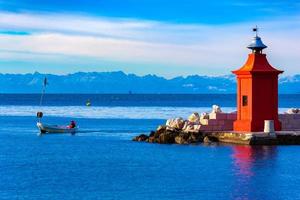 View of the red lighthouse on a pier, a fisherman on a boat and the beautiful mountain range on the horizon, Piran, Slovenia photo