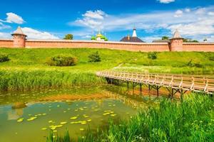 Suzdal cityscape on a summer day. Panorama of the old Russian historic town with traditional architecture and wooden bridge across the river. The Golden Ring of Russia. photo