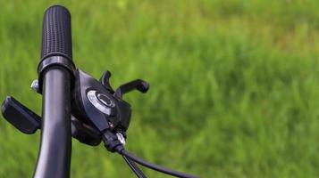 Mountain bike steering wheel on green grass background. Details of sporting events. Close up black mountain bike knob and derailleur knob, left shifter. photo