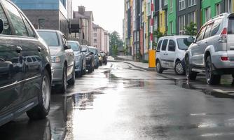 Street in a city without people with parked cars in rainy weather. Rain on the road. Rain and cars. Background of parked cars on a rainy city street. Symmetrical parked cars. photo