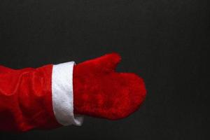 Mock up hand of santa claus in red mittens on a black background. Close-up. New Year concept. copy space photo