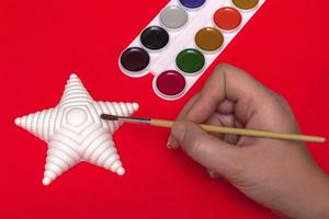 Christmas creativity on a red background woman paints a Christmas star, close-up top view photo