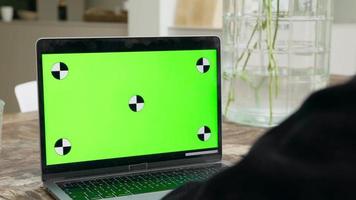 uomo che guarda e scorre su laptop con schermo verde sul tavolo video