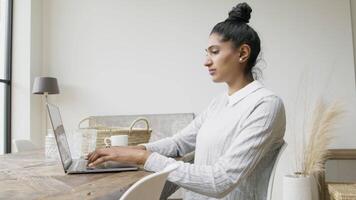 Woman sitting at table thinking and typing on laptop video