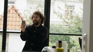 Man standing in kitchen having video call with smartphone