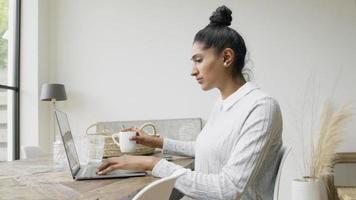 Mujer escribiendo en la computadora portátil tomando un sorbo y pensando
