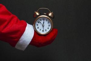 Festive concept. In the hand of santa claus an alarm clock of copper color on a black background. close-up photo