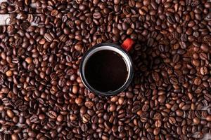 Fondo de granos de café con una taza de metal rojo en el centro con café recién hecho foto