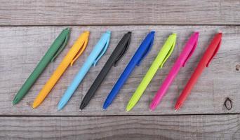 pens of different colors arranged in a row on wooden background photo