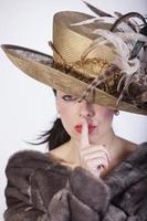 Bella mujer con sombrero y abrigo de piel y el dedo en la boca señalando el silencio
